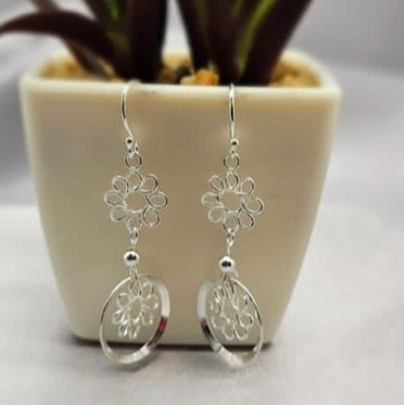 A pair of sterling silver double daisy drop earrings displayed on a table with a plant in the background.