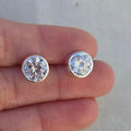 Silver stud earrings held between two fingers against a neutral background