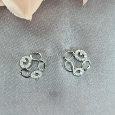 A pair of sterling silver open circle stud earrings with cubic zirconia accents, displayed against a fabric background with a floral motif.