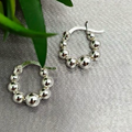 A pair of sterling silver hoop earrings with a hook and balls, displayed on a table with a green leaf and a blurred background.