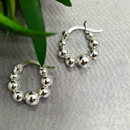 A pair of sterling silver hoop earrings with a hook and balls, displayed on a table with a green leaf and a blurred background.