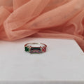 Ring with green and red gemstones on a white surface with pink fabric in the background