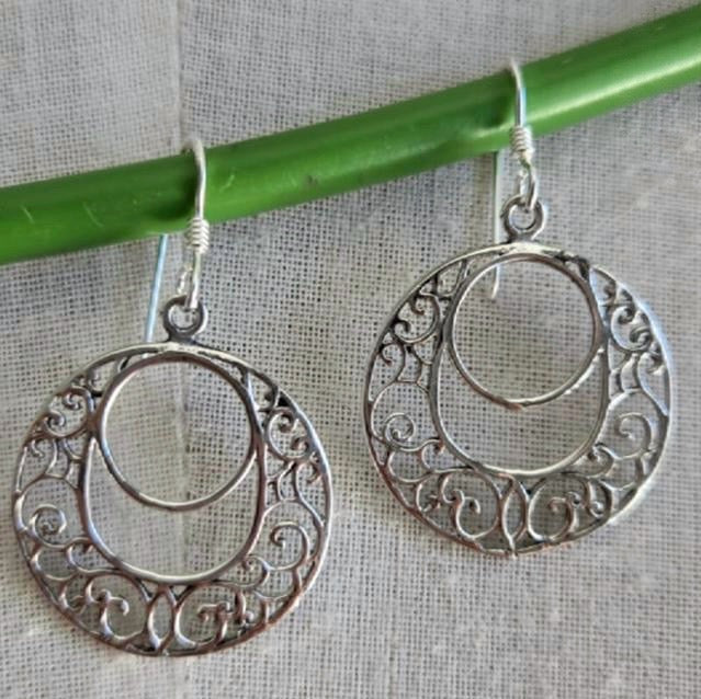 Silver earrings with intricate designs hanging on a green stick against a gray background