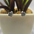 Sterling silver stud earrings in the shape of a rose, displayed in a white pot with a green plant background.