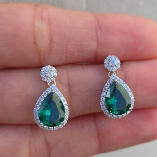 Teardrop-shaped green gemstone earrings with clear stones on a hand.