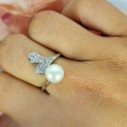 An adjustable sterling silver ring with a pavé heart design on one end and a freshwater pearl on the other, displayed on a person's finger.