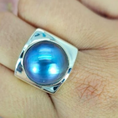A blue mabe pearl ring set in a sterling silver band, displayed on a person's hand.