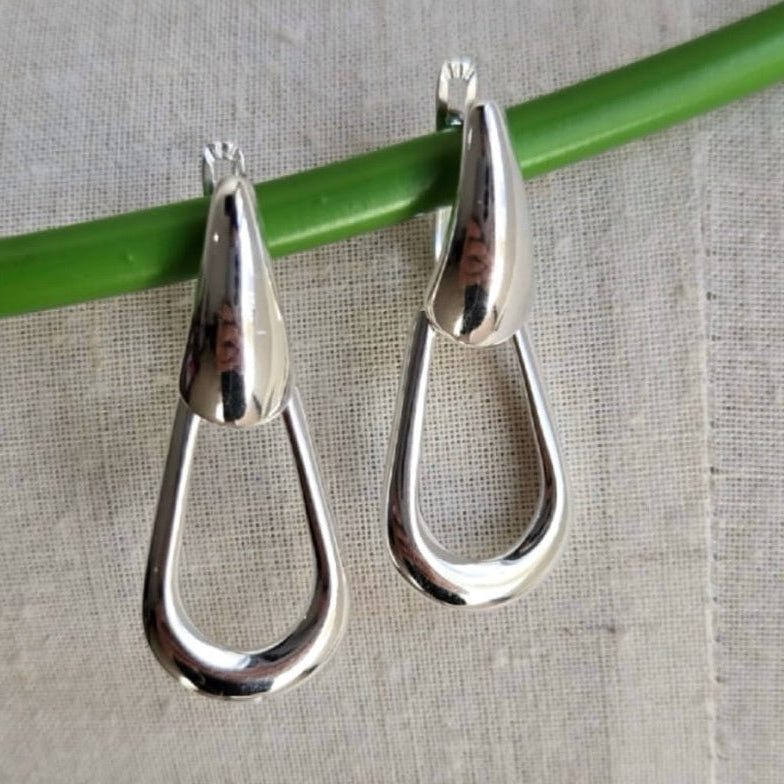 Silver teardrop-shaped earrings on a green stick against a gray background