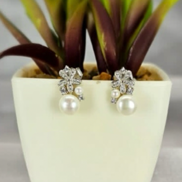 A pair of freshwater pearl earrings with a detailed flower base, displayed in a white vase with a green plant.