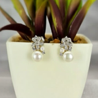 A pair of freshwater pearl earrings with a detailed flower base, displayed in a white vase with a green plant.
