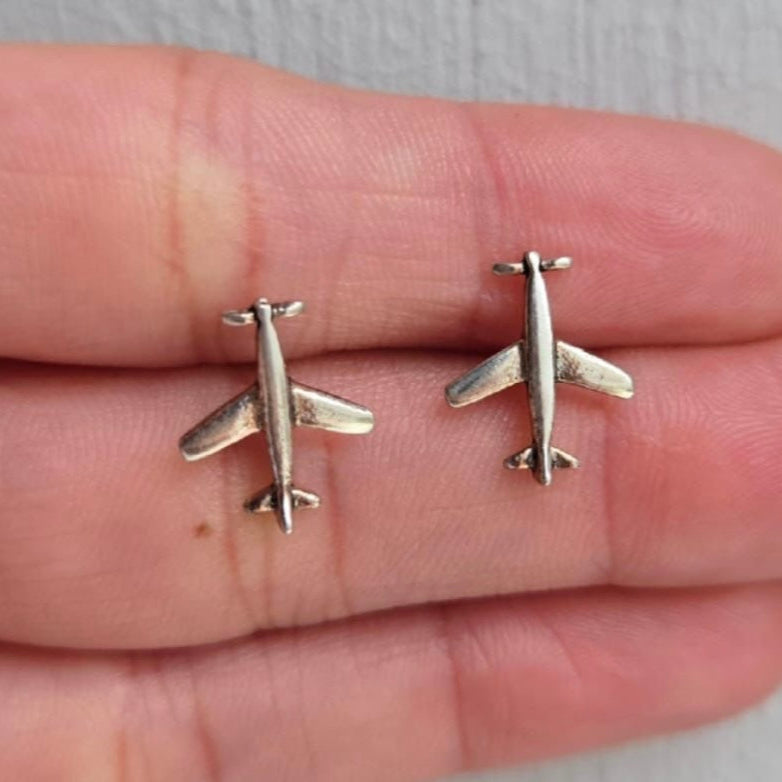 Silver airplane-shaped earrings on a hand