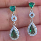 Green gemstone earrings held between fingers