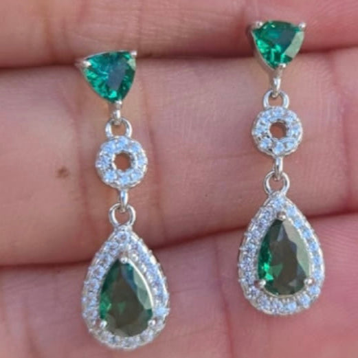 Green gemstone earrings held between fingers