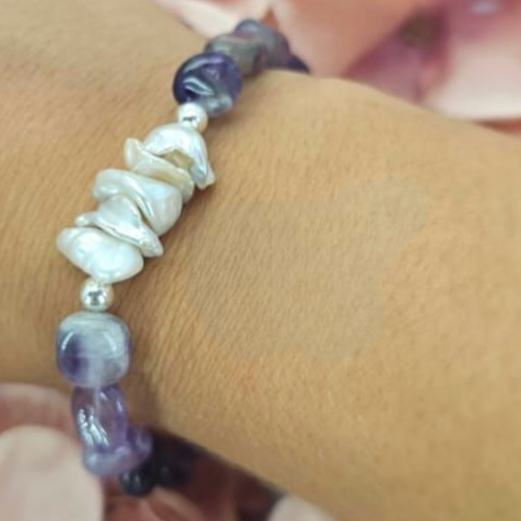 A bracelet featuring beads of semi-precious stones and freshwater pearls, displayed on a person's wrist.