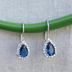 Teardrop-shaped blue gemstone earrings with silver hooks on a green and gray background