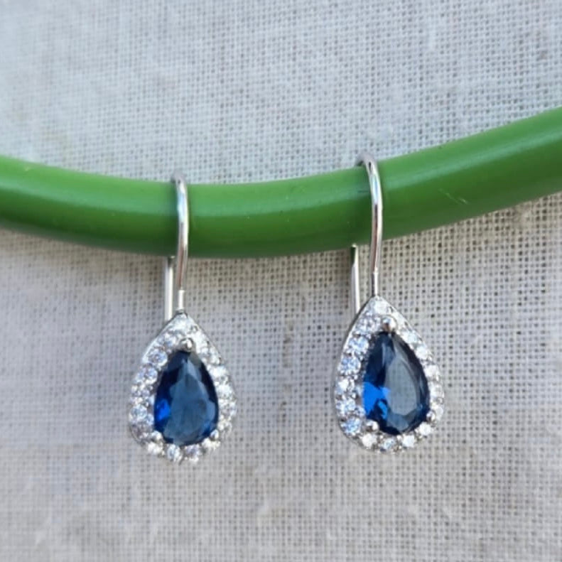 Teardrop-shaped blue gemstone earrings with silver hooks on a green and gray background