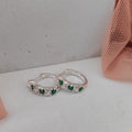 Silver hoop earrings with green gemstones on a white surface.