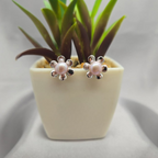 Pair of pearl flower earrings next to a small potted plant on a light gray background