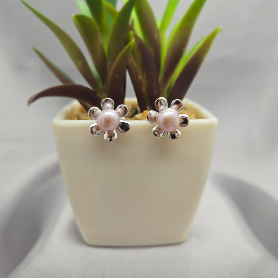 Pair of pearl flower earrings next to a small potted plant on a light gray background