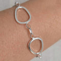 Silver bracelet with interlocking circular links on a wrist against a neutral background