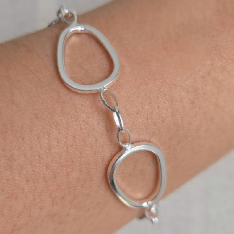 Silver bracelet with interlocking circular links on a wrist against a neutral background