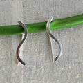 Silver earrings on a green rod against a textured gray background