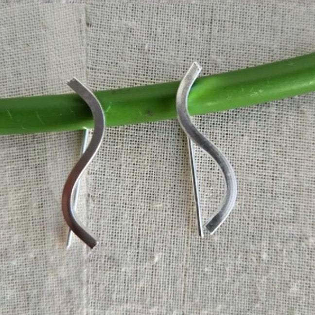 Silver earrings on a green rod against a textured gray background