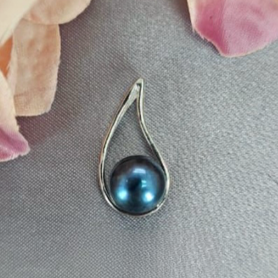 A teardrop-shaped blue freshwater pearl pendant set in sterling silver, displayed against a fabric background with floral accents.