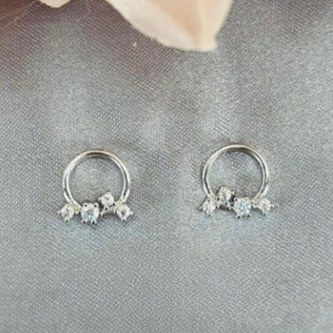 A pair of sterling silver circle stud earrings with cubic drops, displayed against a neutral background with a floral pattern.
