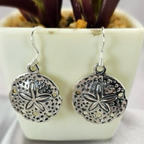 Round drop earrings with a starfish pattern, made of sterling silver, displayed in a white container with a green plant in the background.