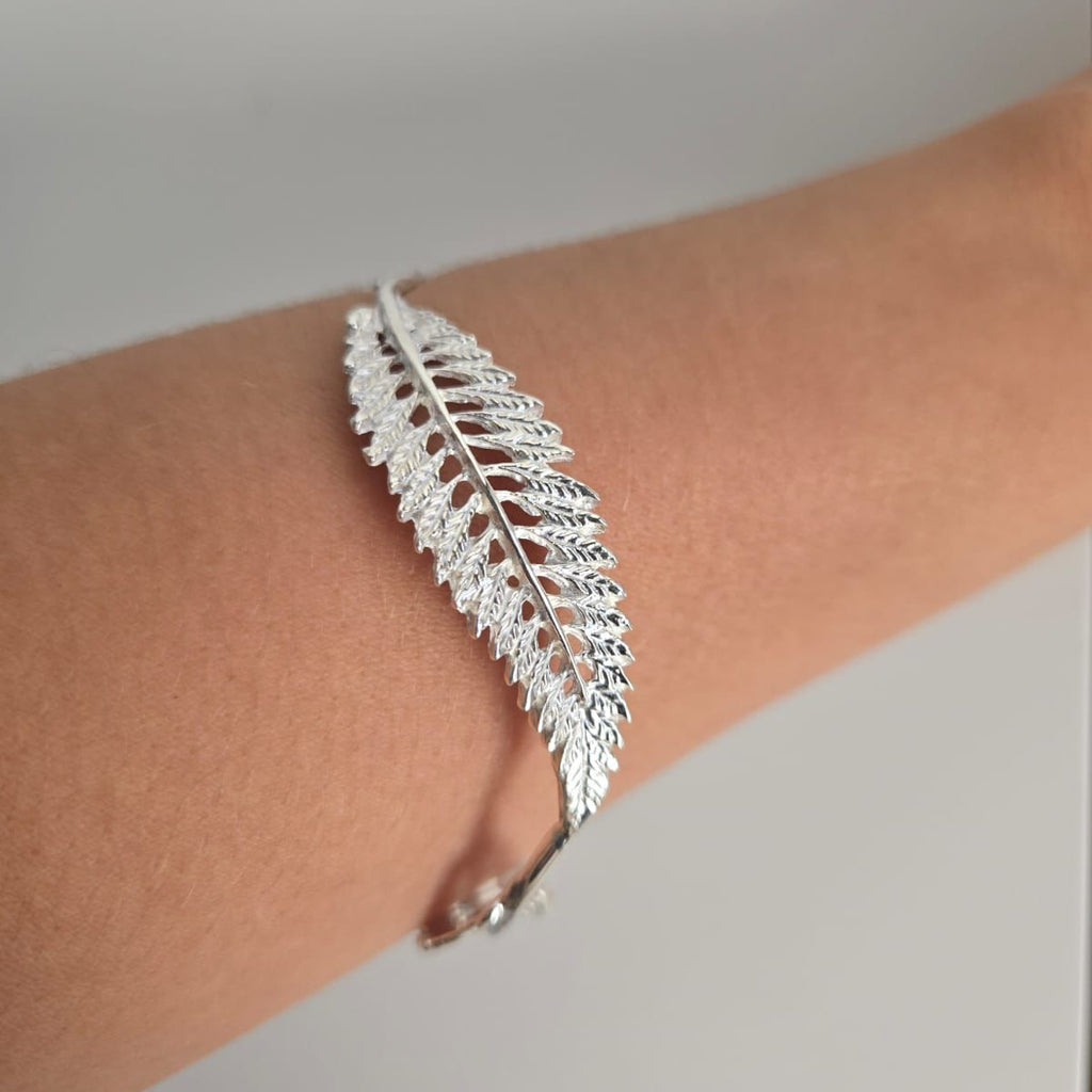 Silver feather-shaped bracelet on a wrist against a neutral background