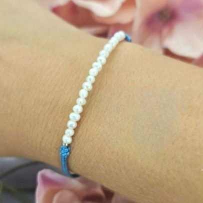 A bracelet featuring tiny freshwater pearls on an adjustable blue cord, displayed on a person's wrist.