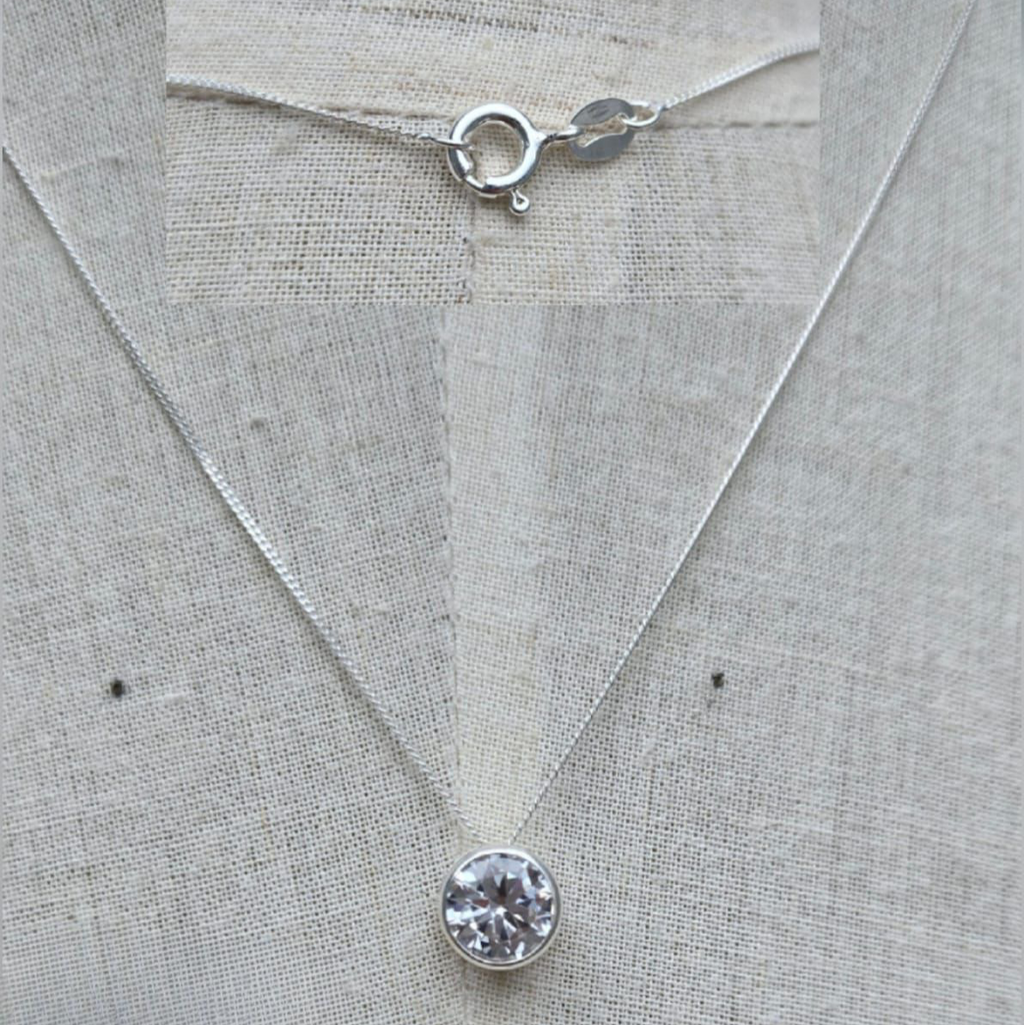 Silver necklace with a round pendant on a light gray fabric background