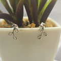 A pair of silver open leaf stud earrings displayed in a white vase with green plant leaves.