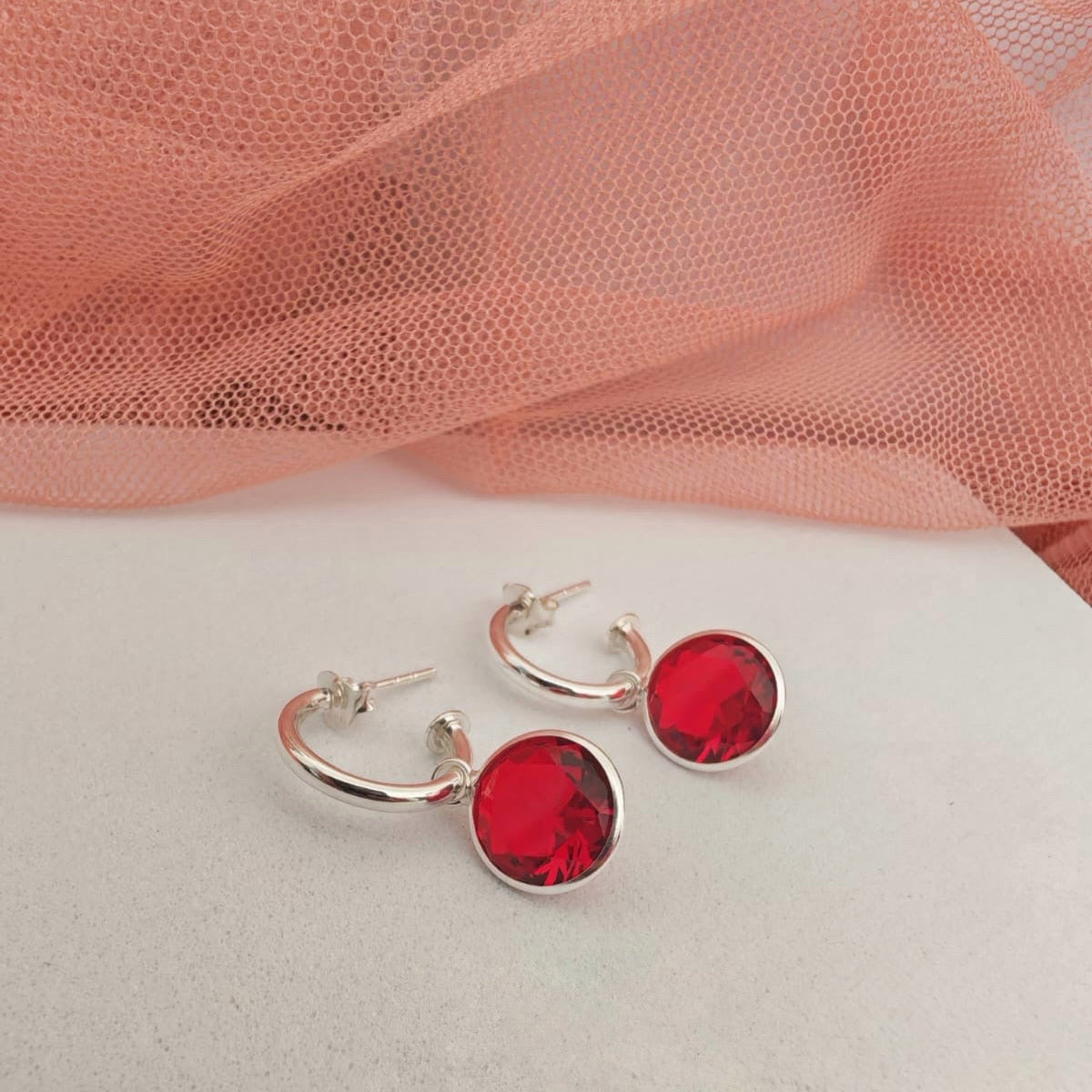 Silver hoop earrings with red gemstones on a light pink fabric background