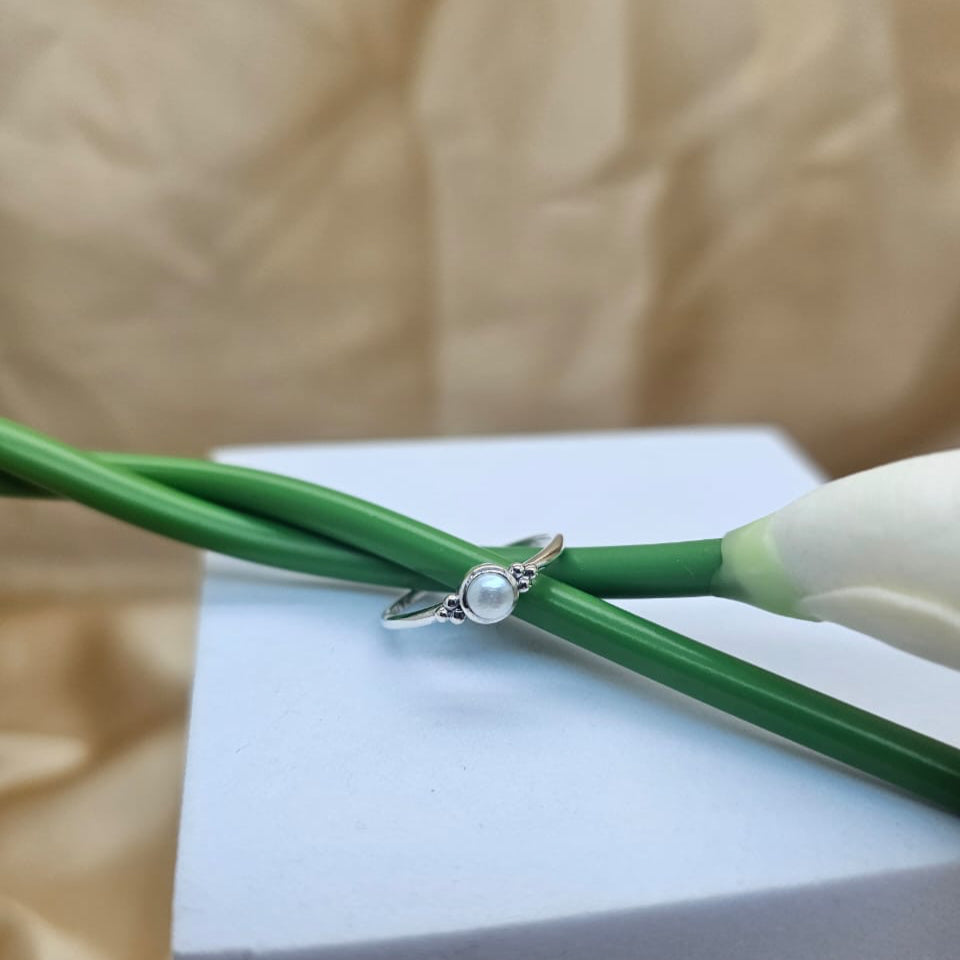 Silver ring with a pearl on a white block with green stems in the background