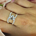 A sterling silver open ring with a knot design worn on a person's finger.