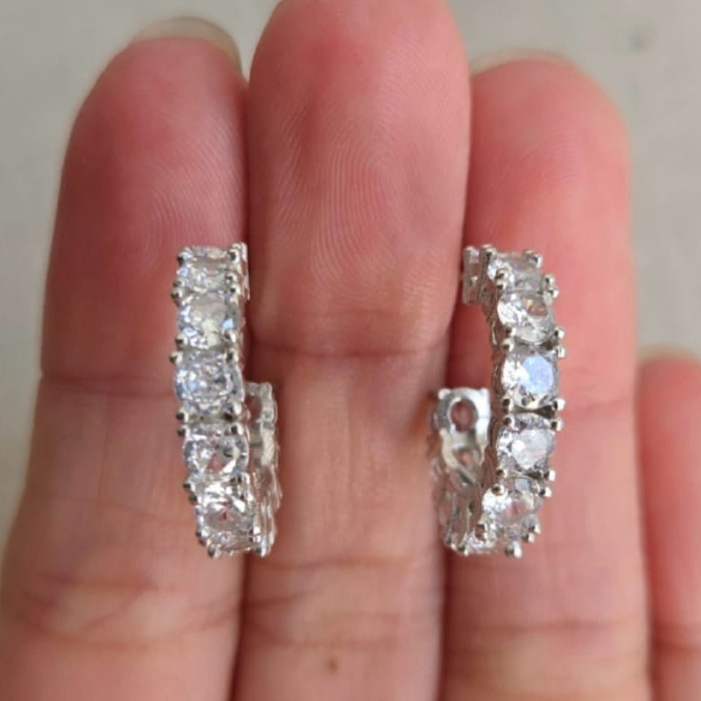 Silver hoop earrings held between fingers against a neutral background