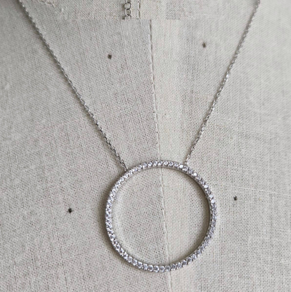Silver necklace with a circular pendant on a light gray fabric background