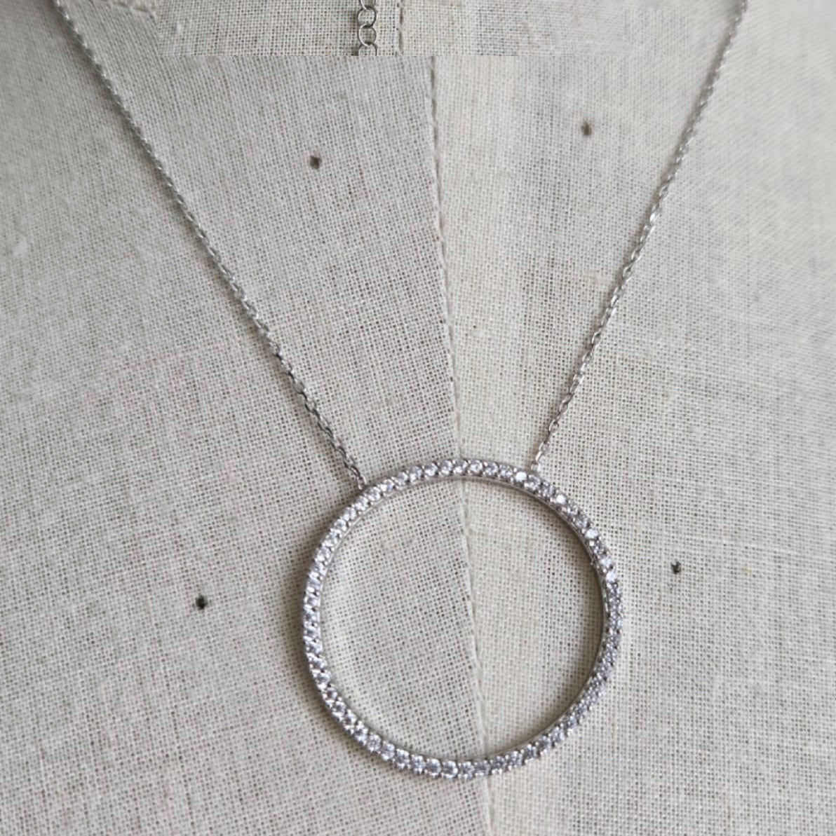 Silver necklace with a circular pendant on a light gray fabric background