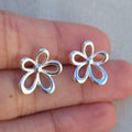 Silver flower-shaped earrings held between fingers against a neutral background