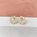 Gold hoop earrings with clear stones on a light pink fabric background