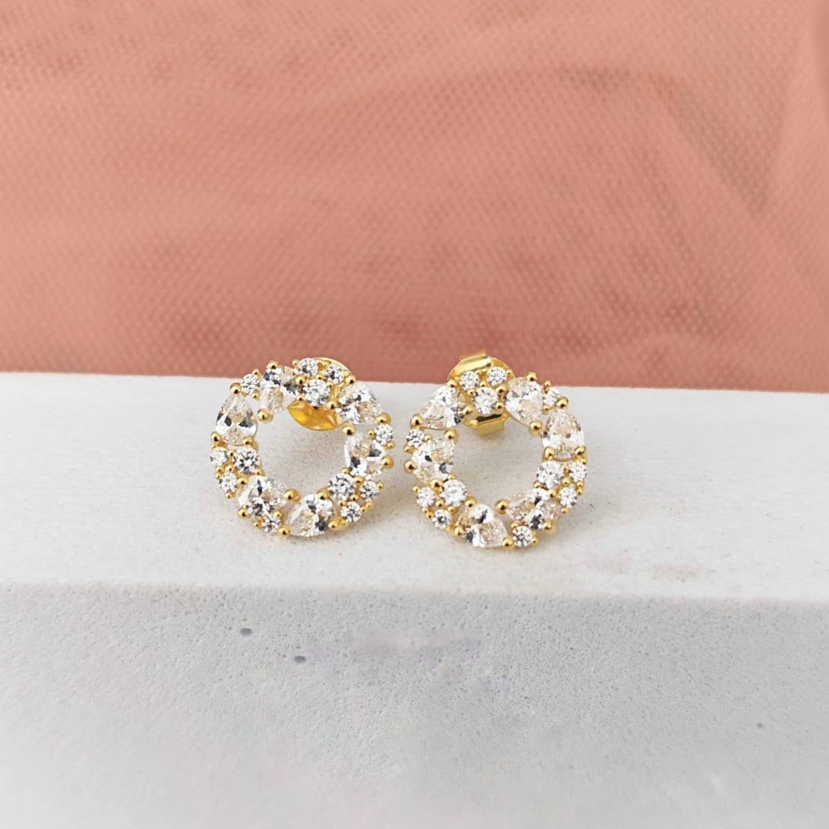 Gold hoop earrings with clear stones on a light pink fabric background