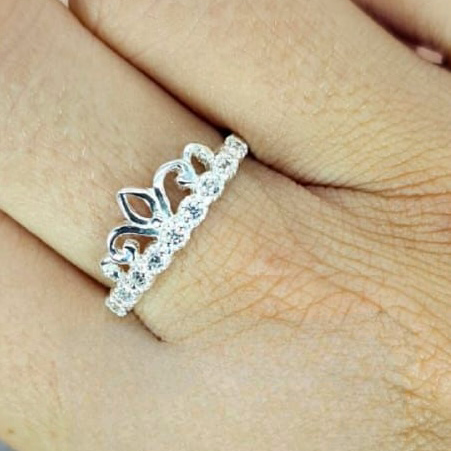 A sterling silver ring with a crown design, featuring cubic zirconia, worn on a person's hand.