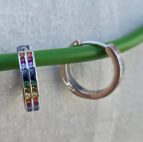 Silver hoop earrings with colorful gemstones on a green stick against a gray background