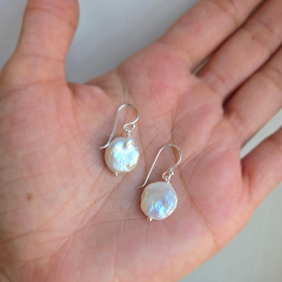 A pair of sterling silver coin pearl drop earrings held in a person's hand.