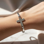 Silver cross bracelet on a wrist against a neutral background