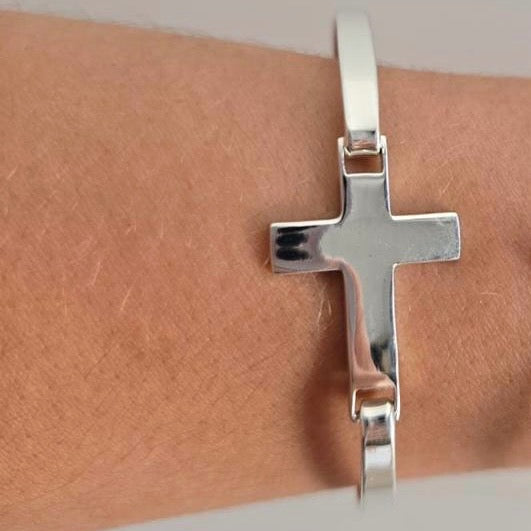 Silver cross bracelet on a wrist against a neutral background