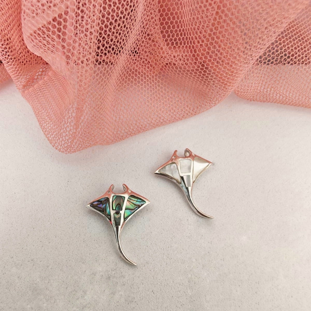 Manta ray earrings on a white surface with pink fabric in the background