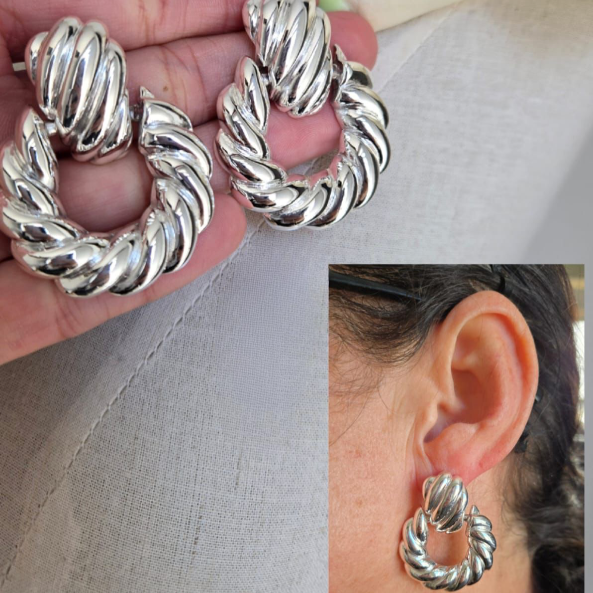 Silver hoop earrings held in hand and worn on an ear against a neutral background